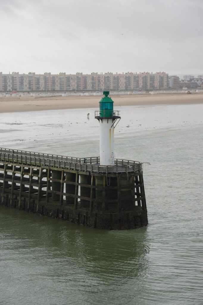 Foto  a vista de pajaro del Faro de Calais. 
 De color blanco y con el tejadillo verdoso, y al fondo la ciudad